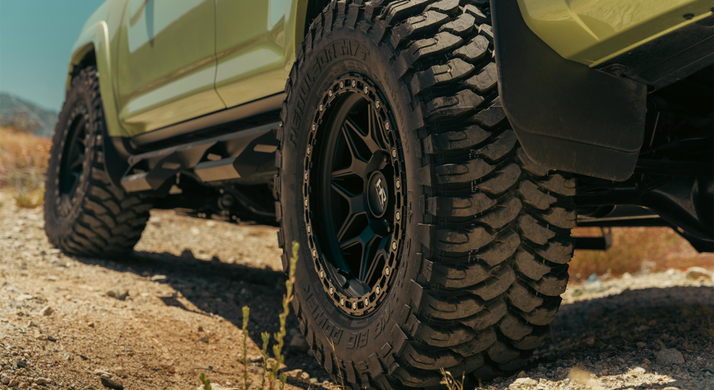 A green Toyota Tacoma parked on a dirt road, showcasing its front end and rugged design against a natural backdrop.